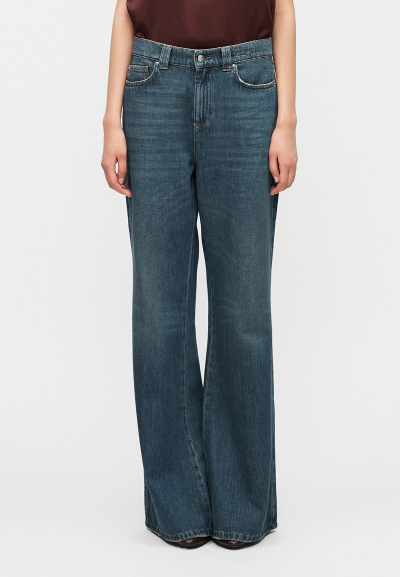 Τζιν παντελόνι σε σκούρο μπλε χρώμα, σχεδίαση με φαρδιά πόδια, με μπροστινές τσέπες και κούμπωμα με κουμπί. Το ύφασμα έχει φθαρμένο υφή με διακριτικές ξεθωριασμένες περιοχές.