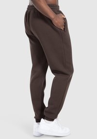 Braune Sweatpants mit einer lockeren Passform, elastischem Bund, Seitentaschen und gerippten Bündchen, kombiniert mit weißen Sneakern.