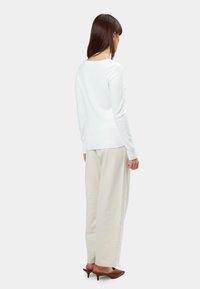 Weißer Strickpullover mit geripptem Saum, kombiniert mit cremefarbenen weit geschnittenen Hosen. Das Model trägt braune modische Mules, von hinten gesehen.