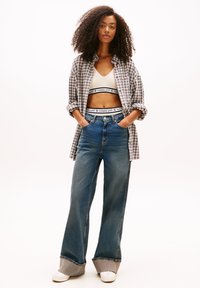 Camicia a quadri grigia, blu e bianca indossata sopra un crop top color crema, abbinata a jeans a gamba larga blu con orlo grigio risvoltato e sneakers bianche.