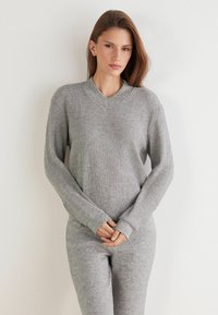 Grau gestreifter Strickpullover mit V-Ausschnitt und langen Ärmeln, kombiniert mit passenden grauen Hosen. Der Stoff wirkt weich und strukturiert.
