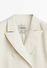 Blazer croisé couleur crème avec de larges revers et des boutons blancs, étiqueté Massimo Dutti Limited Edition, fabriqué au Portugal.