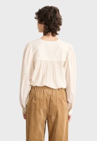 Cream blouse with billowy sleeves and back pleats, paired with beige corduroy trousers featuring an elastic waistband and vertical stripes.