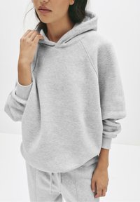 Felpa grigia in morbido tessuto con cappuccio spazioso, maniche raglan, polsini a costine e vestibilità rilassata, abbinata a pantaloni della tuta coordinati.