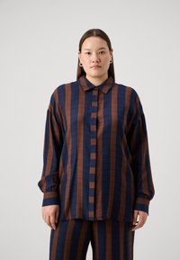 Tamsiai mėlynas ir rudas dryžuotas marškinis, pagamintas iš lengvos medžiagos. Turi apykaklę ir ilgomis rankovėmis su rankogalių detalėmis.