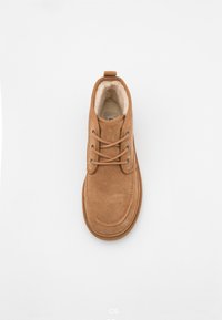 Stivale alla caviglia in suede marrone con punta rotonda, design con lacci e morbida fodera in pile. Presenta un passante sul retro e dettagli di cucitura sulla suola.