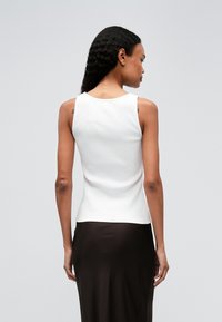 Witte ribbel tanktop met een ronde halslijn, een aansluitend ontwerp en een gladde textuur; gestyled met een donkerbruine rok op een neutrale achtergrond.