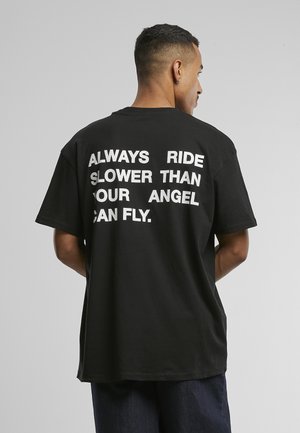 Mann sett bakfra iført svart T-skjorte med hvit tekst: "Kjør alltid saktere enn engelen din kan fly."