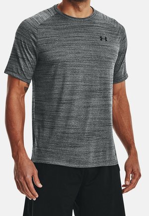 Mann trägt ein meliertes graues, kurzärmeliges Sportshirt mit kleinem schwarzen Under Armour-Logo auf der linken Brust und schwarze Shorts.