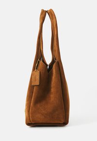 Bruine suède hobo tas met dubbele hengsels, ronde bovenkant en een ritsluiting. Voorzien van een klein label dat met een gouden ketting is bevestigd. Zachte textuur.