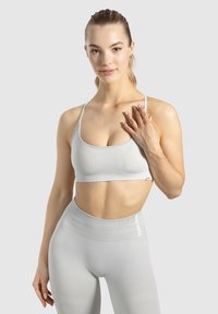 Hellgrauer Sport-BH aus strukturiertem Stoff mit dünnen Trägern, kombiniert mit hochtaillierten grauen Leggings, die ein Logo am Bund tragen.