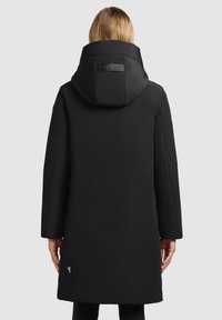 Zwarte parka met een ruime capuchon, gemaakt van glad materiaal, met een logopatch op de achterkant en een knie-lange snit zonder zichtbare sluitingen.