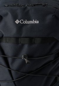 Μαύρο σακίδιο πλάτης Columbia με υφασμάτινη υφή, ελαστικές μπαντζάρι λεπτομέρειες και λογότυπο κεντημένο σε λευκό στο πάνω μέρος.