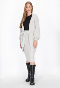 Lichtgrijze gebreide cardigan met een strik taille, gecombineerd met een bijpassende rok en zwarte kniehoge laarzen. Zachte textuur en een comfortabele pasvorm.