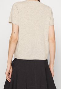 Beige kortærmet sweater lavet af blødt strikstof, med et enkelt, tætsiddende design, rund halsudskæring og let forkortet kant.