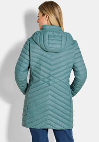 Lichtblauwe geïsoleerde jas met een chevron-quiltpatroon, een capuchon en lange mouwen. Het ontwerp van de achterkant heeft horizontale naden voor textuur.