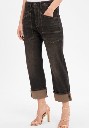 Dunkelblaue Jeans mit lässiger Passform, umgeschlagenen Säumen und zwei Fronttaschen. Betont mit kontrastierendem Stoff an den Säumen und Nähdetails.