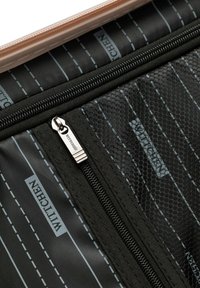 Zwart en grijs gestreepte stof met een gemerkte metalen ritsen trekker gelabeld "Wittchen" op een binnenzak van de tas.