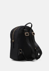 Sac à dos noir avec une texture lisse, fermeture éclair dorée et sangles en tissu réglables. Doté d'une poignée supérieure et d'une poche latérale. Design simple.
