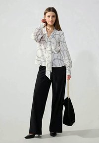 Valkoinen pusero, jossa musta ketjukuosi, solmittava edestä, liehuvat hihat. Yhdistetty mustiin leveälahkeisiin housuihin ja mustaan samettiseen laukkuun. Mustat teräväkärkiset kengät.