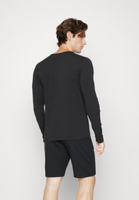 Schwarzes Langarmshirt aus weichem Stoff, mit rundem Halsausschnitt und schmaler Passform, kombiniert mit schwarzen Shorts für einen stimmigen Look.