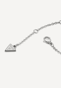 Braccialetto in argento con un charm triangolare con la parola "GUESS" incisa, e chiusura a moschettone.