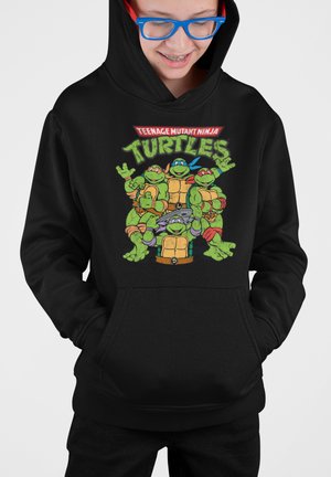Schwarzer Hoodie mit einem bunten Grafik von vier Cartoon-Schildkröten, jede in einer anderen Pose, mit dem Text "TEENAGE MUTANT NINJA TURTLES" darüber.