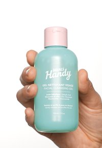 Una bottiglia di plastica turchese con un tappo rosa, etichettata "Merci Handy Gel Nettoyant Visage", contiene 150 ml di gel detergente per il viso.