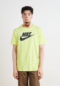 Camiseta de algodón verde lima con un prominente logo negro de Nike en el pecho. Mangas cortas y cuello redondo.