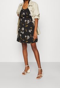 Czarna sukienka w kwiaty z krótkimi rękawami, z zaznaczoną talią i białymi kwiatami. Połączona z beżowymi sandałami na słupku.