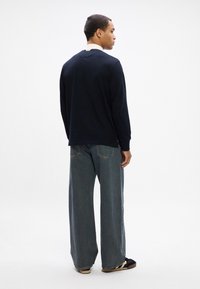 Cămașă în nuanță de bleumarin, cu mâneci lungi și guler în contrast, asociată cu blugi denim cu picioare largi. Textura pare moale, cu detalii minime.