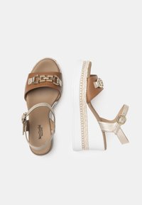 Brown and gold platform sandals with a wide strap, chain detail, and adjustable ankle strap. White rubber sole with jute accent.
