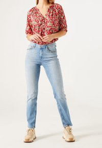 Red floral blouse with short sleeves, paired with light blue skinny jeans. Beige sneakers with textured pattern complete the outfit.