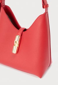 Czerwona skórzana torba na ramię o teksturowanej powierzchni, charakterystycznym kanciastym kształcie oraz złotym zapięciu. Dołączony regulowany pasek.