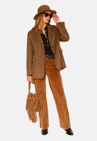 Blazer en tweed marron porté sur un blouse noire, associé à un pantalon large en velours côtelé marron. Accessoirisé avec un sac à franges et un chapeau à larges bords.