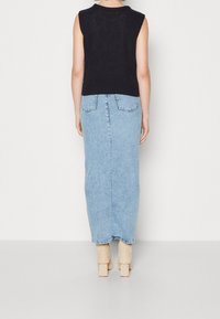 Svart stickad ärmlös topp tillsammans med en ljusblå denim maxikjol. Beiga klackstövlar vid vristen fulländar outfiten.