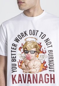 Biely bavlnený tričko s farebnou grafikou cherubínskej postavy s aureolou a slnečnými okuliarmi, a textom: "LEPŠIE CVIČ, ABY SI SA NEZAPÁLIL KAVANAGH."
