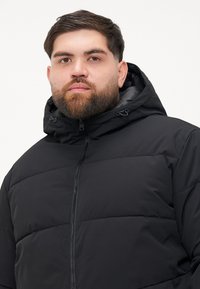 Black padded jacket with a zip closure and adjustable hood. Features a textured surface and horizontal quilted pattern for insulation.