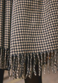 Woven woolen scarf featuring a navy and cream check pattern, with a fringed edge for texture and detail.