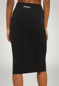 Jupe noire en tissu extensible. Dotée d'une taille élastique et d'un petit logo blanc à l'arrière. Texture lisse, coupe ajustée.