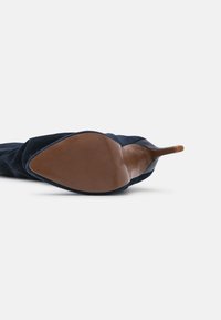 Chaussure à talon haut en daim bleu marine avec un bout pointu, dotée d'une semelle marron lisse avec un motif antidérapant texturé.