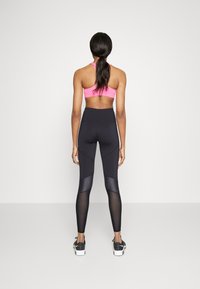 Sportbeha in felroze met een racerback ontwerp en hoge zwarte leggings met mesh-panelen en geometrische patroonaccenten.