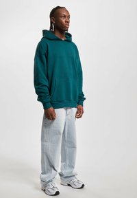 Tökéletes méretű, türkiz oversized kapucnis pulóver kenguru zsebbel, világoskék széles szárú farmernadrággal és szürke sportcipővel párosítva. Egyszerű dizájn, laza szabás.