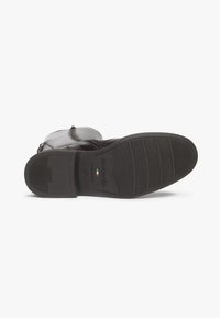 Semelle en cuir marron avec un dessous en caoutchouc texturé. Comprend un logo et des lignes horizontales pour l'adhérence. Design à bout rond.