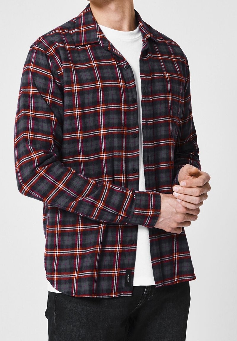 Camisa de franela a cuadros en colores rojo, naranja y negro. Diseño con botones y mangas largas; se lleva sobre una camiseta blanca. Corte casual.