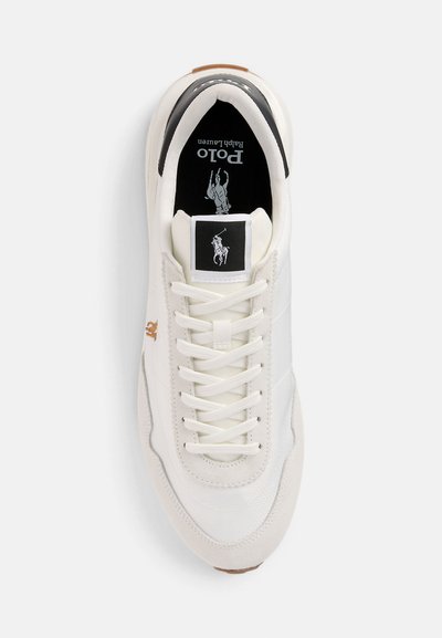 Witte sneaker met gestructureerde stof en gladde leren details. Heeft een zwart-wit logo-opdruk op de tong en lichtbruine accenten op de zool.