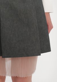 Jupe en denim gris avec un sous-vêtement nude plissé, présentant une finition texturée et un design superposé. Taille visible et détails de l'ourlet contrastants.
