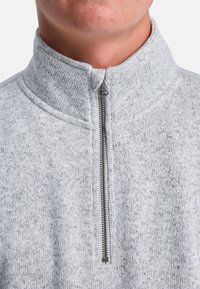 Sudadera de forro polar gris con cremallera, de cuello alto, que presenta una cremallera plateada y un patrón texturizado en todo el tejido.