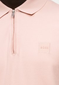 Ανοιχτό ροζ πόλο μπλούζα με φερμουάρ και ανάγλυφο λογότυπο "BOSS" στο αριστερό στήθος.