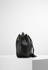 Svart läderhinkväska med detaljer i guld, snörstängning och en texturerad yta. Har en lång axelrem och en fransdetalj.